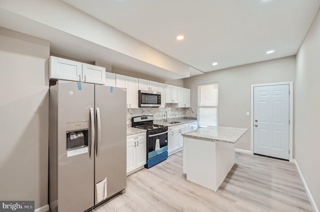 kitchen with light wood-type flooring, stainless steel appliances, a kitchen island, and white cabinets