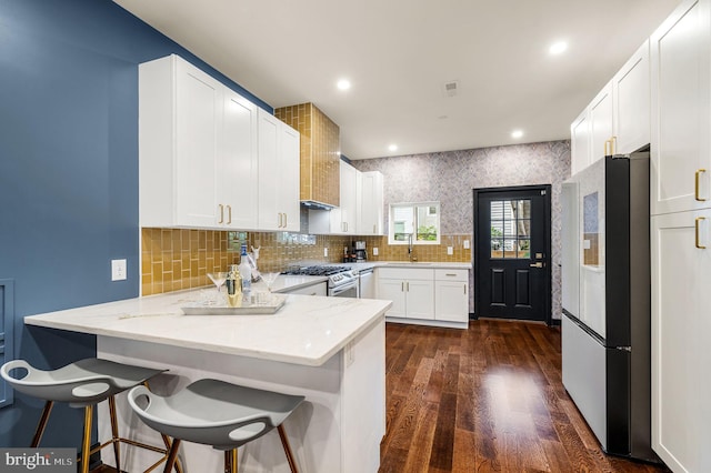 kitchen featuring stainless steel gas range oven, fridge, dark wood-type flooring, light stone countertops, and kitchen peninsula