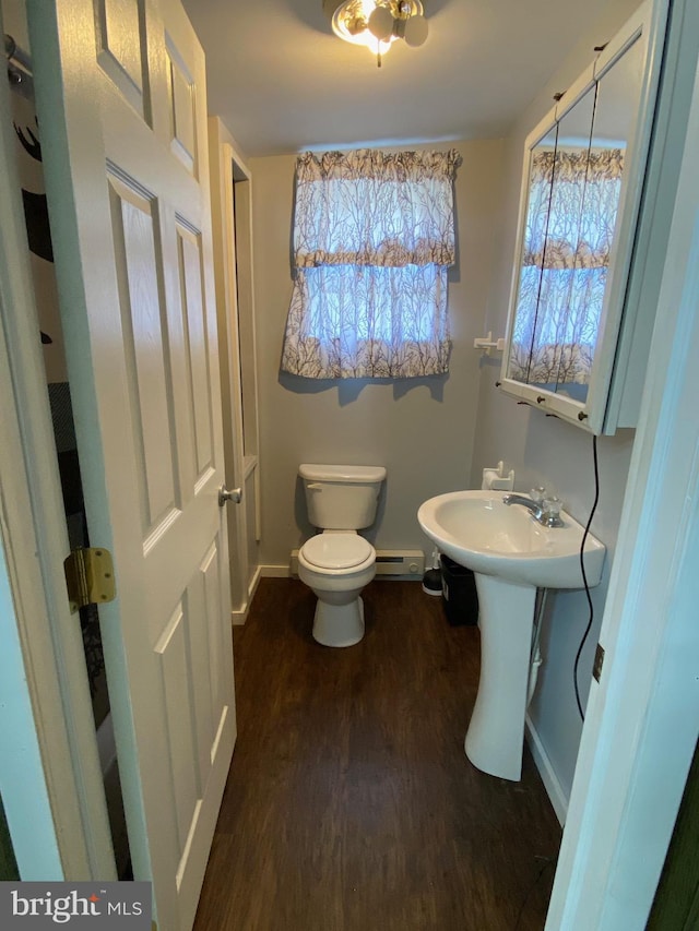 half bathroom featuring toilet, a baseboard heating unit, a sink, wood finished floors, and baseboards