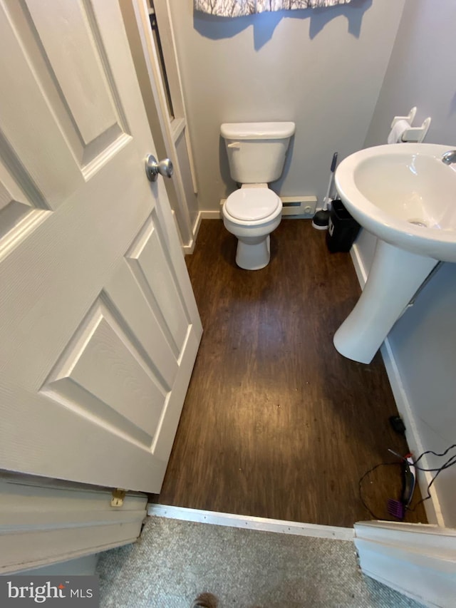 half bathroom featuring baseboard heating, baseboards, toilet, and wood finished floors