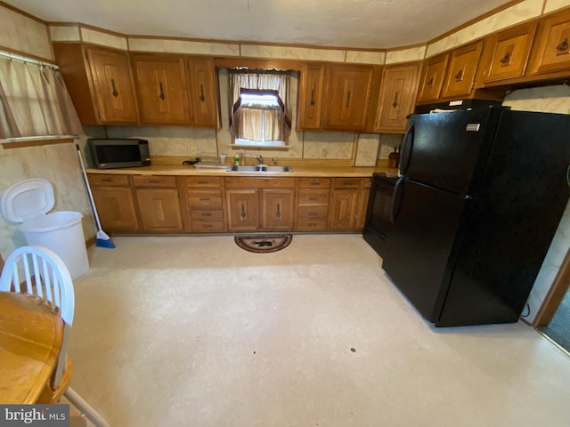 kitchen with light countertops, a sink, freestanding refrigerator, and brown cabinets