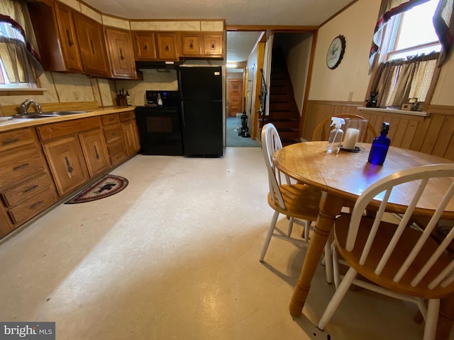 kitchen with a wainscoted wall, brown cabinets, light countertops, black appliances, and a sink