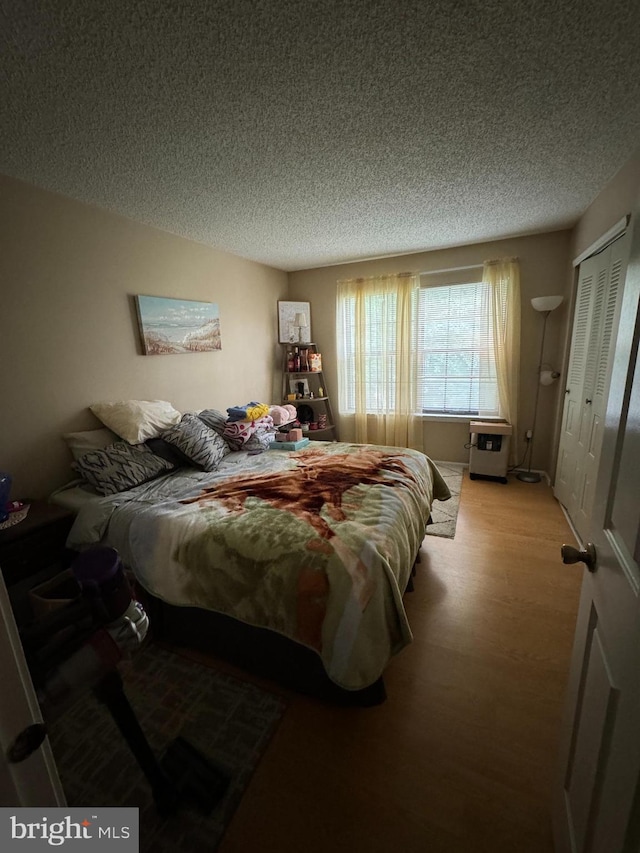 bedroom with a textured ceiling, hardwood / wood-style floors, and a closet