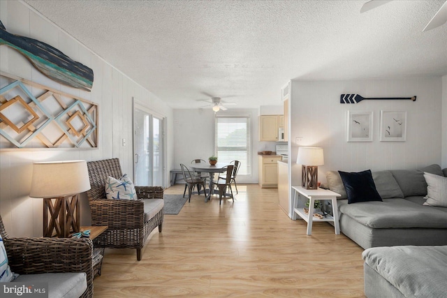 living room featuring ceiling fan, light hardwood / wood-style flooring, and a textured ceiling