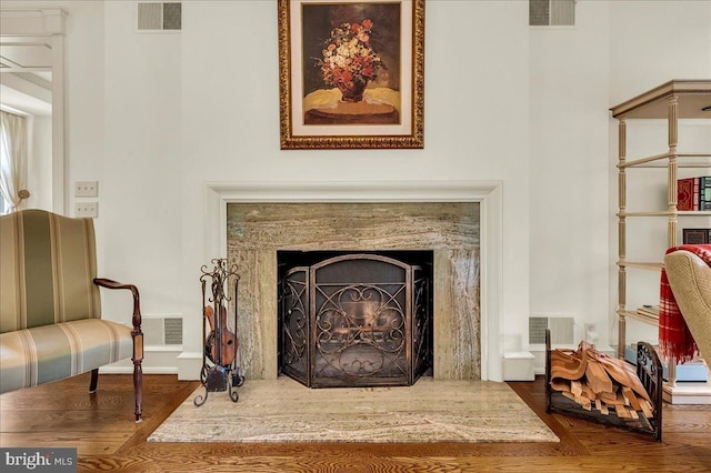 living area featuring visible vents, wood finished floors, and a high end fireplace