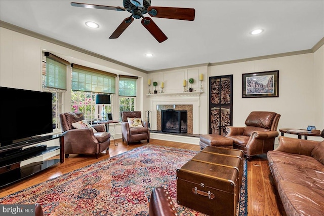 living area with ceiling fan, a premium fireplace, wood finished floors, crown molding, and recessed lighting