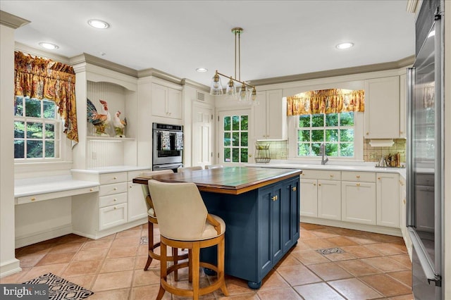 kitchen featuring built in study area, a center island, decorative light fixtures, stainless steel appliances, and a kitchen bar