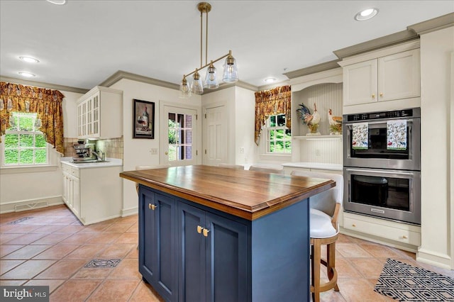 kitchen featuring butcher block counters, glass insert cabinets, hanging light fixtures, stainless steel double oven, and blue cabinetry