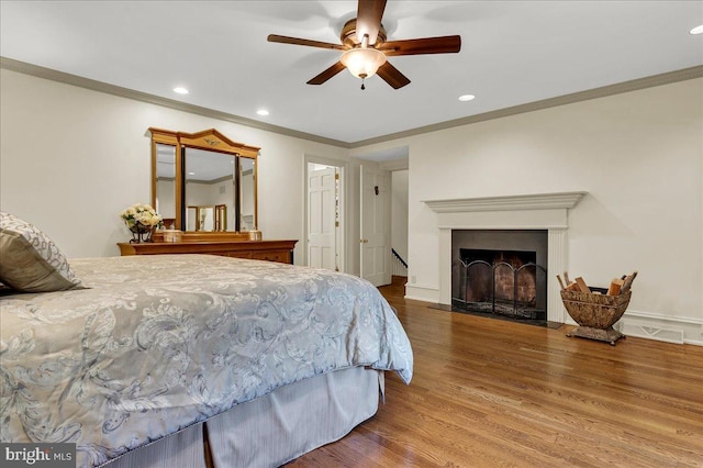 bedroom featuring recessed lighting, a fireplace with flush hearth, ornamental molding, wood finished floors, and baseboards