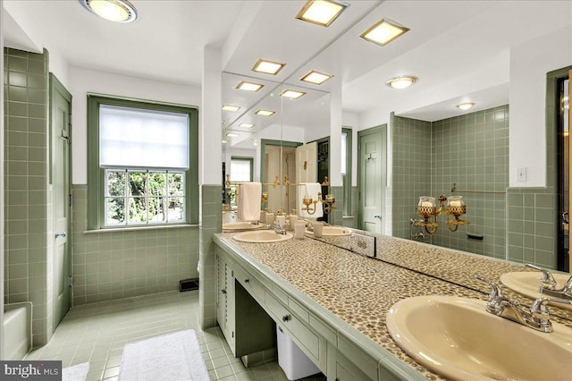 full bath with double vanity, tile patterned flooring, a sink, and tile walls