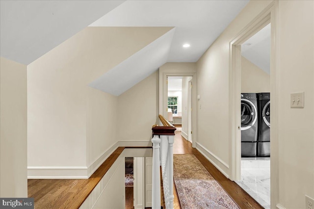 corridor with lofted ceiling, washing machine and clothes dryer, wood finished floors, and an upstairs landing