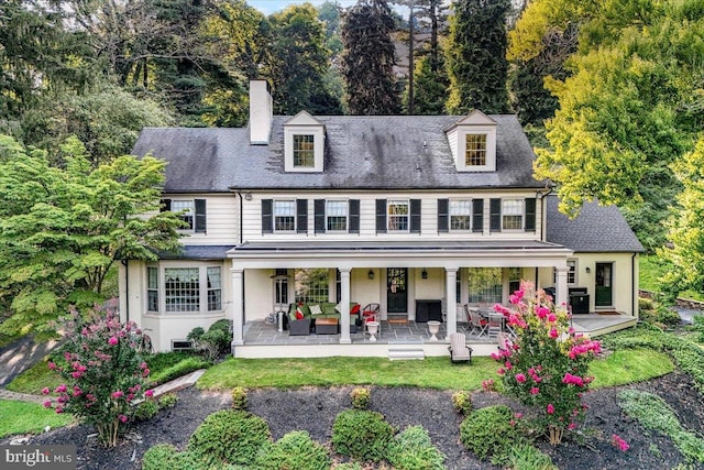 back of property featuring a patio area, a chimney, an outdoor living space, and roof with shingles