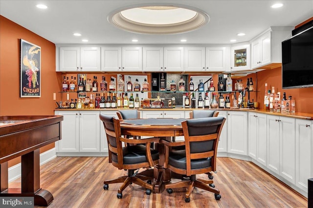 interior space with a dry bar, light wood finished floors, a tray ceiling, and recessed lighting