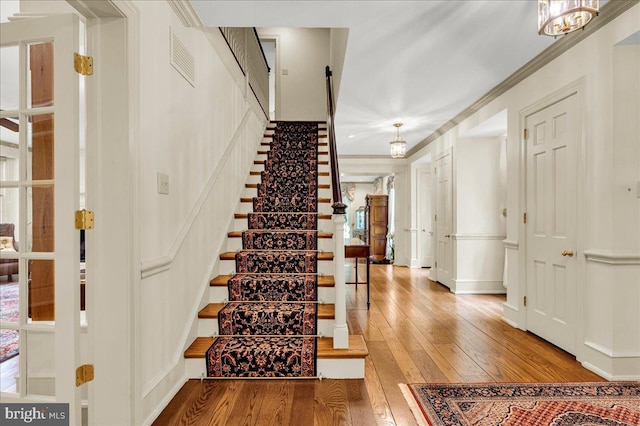 stairway with baseboards, visible vents, crown molding, and wood finished floors