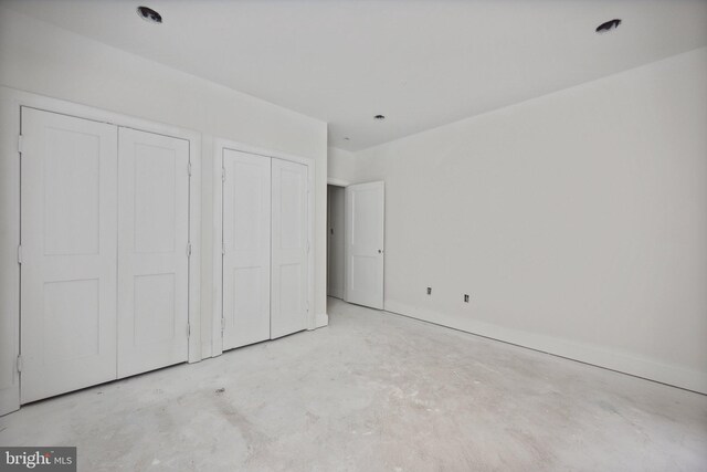 unfurnished bedroom with baseboards, concrete floors, and multiple closets