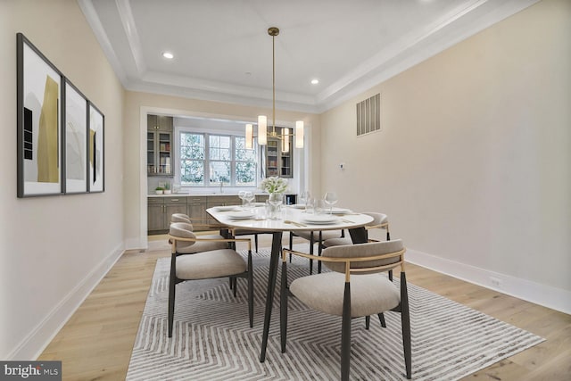 dining space with light wood-style floors, baseboards, visible vents, and a raised ceiling