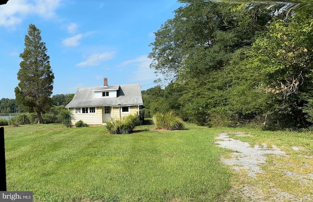 exterior space featuring driveway, a chimney, and a lawn