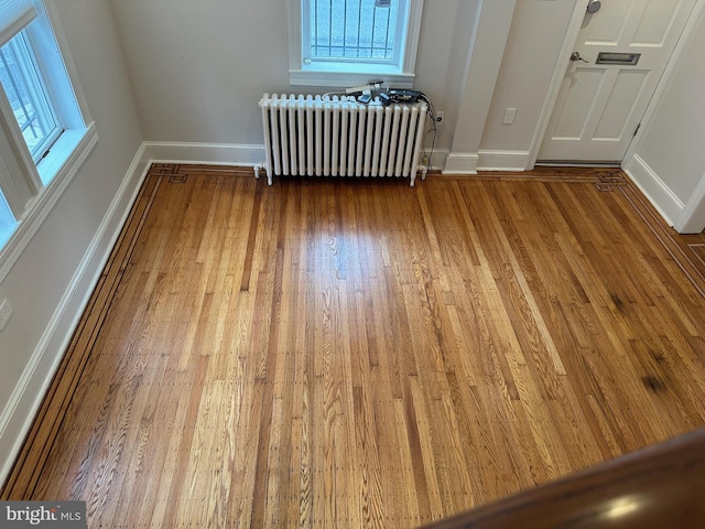 empty room with a healthy amount of sunlight, radiator, baseboards, and wood finished floors