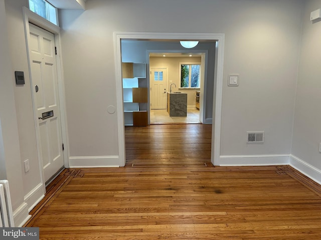 hall featuring a sink, visible vents, baseboards, and wood finished floors