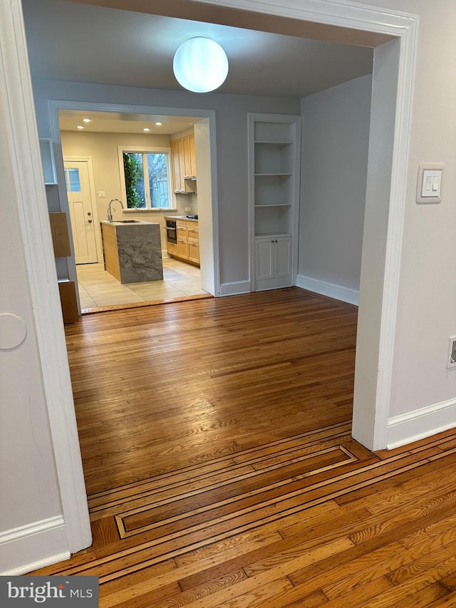 interior space featuring light wood-style flooring, built in features, baseboards, and a sink