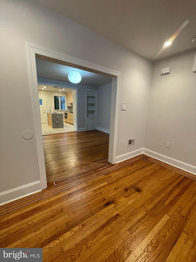 empty room with visible vents, wood-type flooring, and baseboards