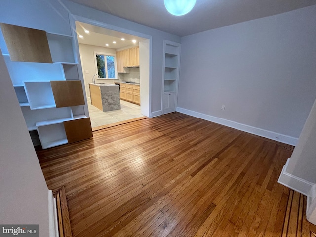 unfurnished living room with built in features, baseboards, light wood finished floors, and a sink