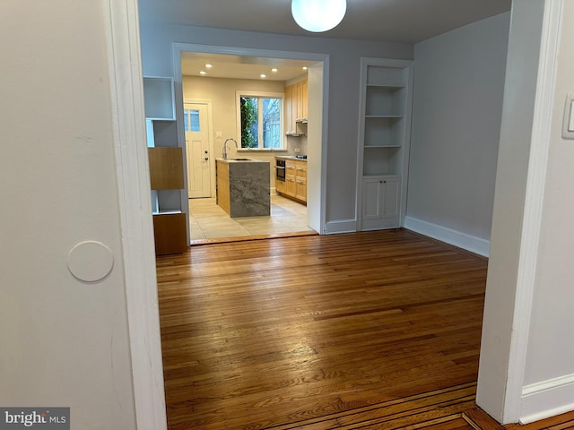 corridor with light wood finished floors, built in shelves, baseboards, and a sink