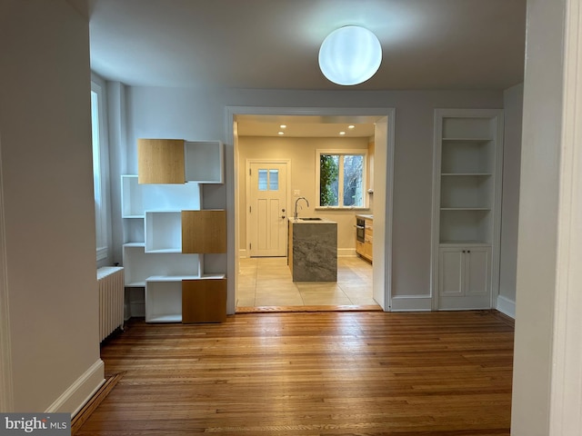 interior space with built in features, a sink, radiator heating unit, light wood-style floors, and baseboards