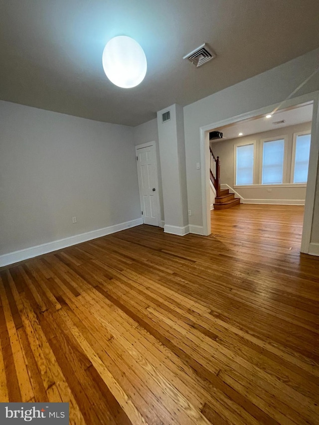 empty room featuring stairs, hardwood / wood-style flooring, baseboards, and visible vents