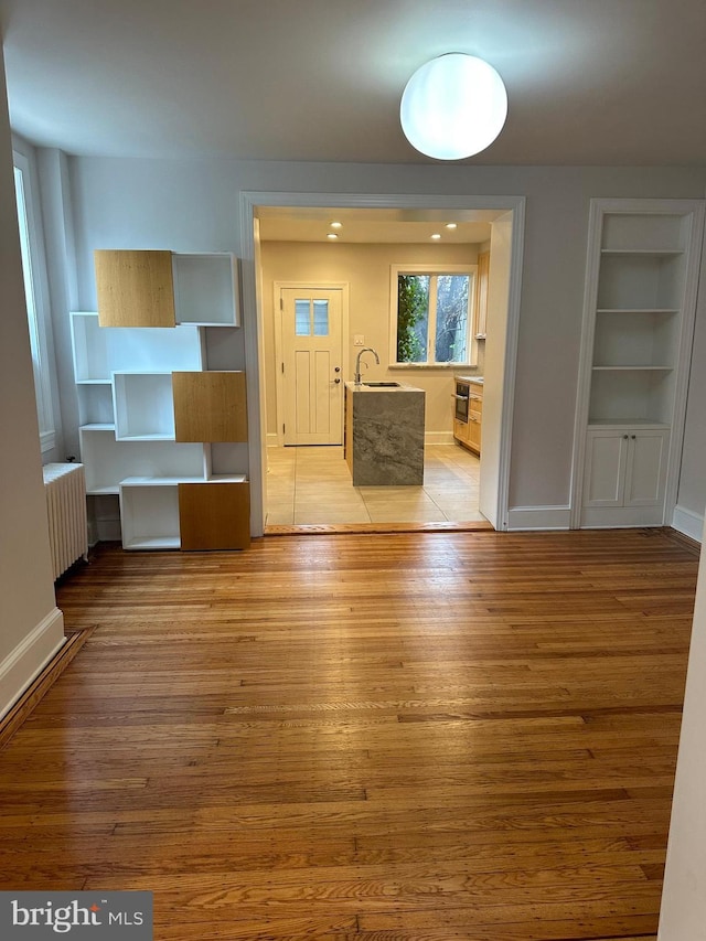 interior space with built in shelves, radiator, baseboards, light wood-style floors, and a sink