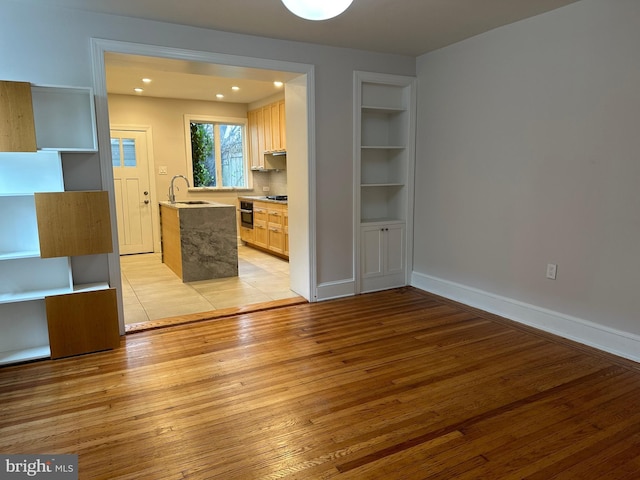 unfurnished dining area with light wood finished floors, built in shelves, baseboards, recessed lighting, and a sink