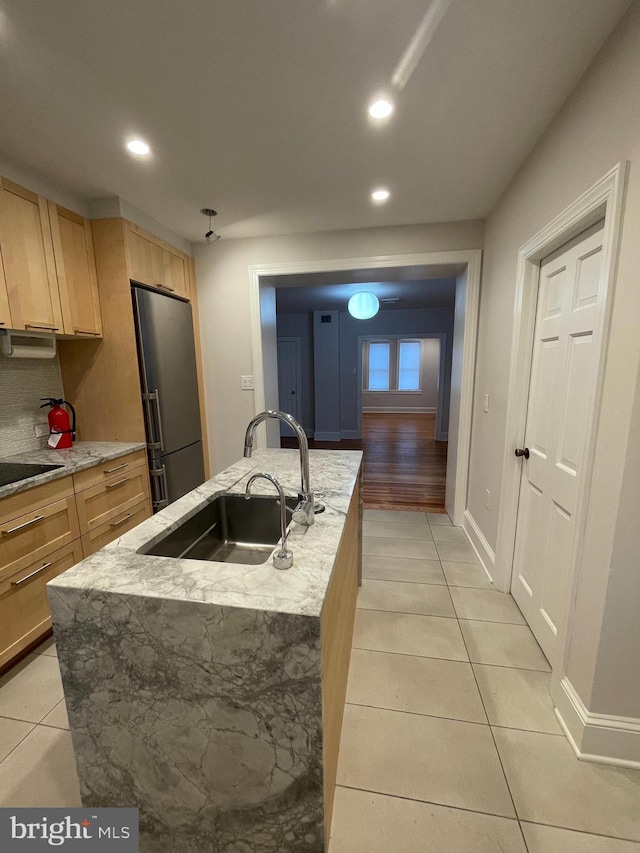 kitchen featuring light brown cabinetry, light tile patterned floors, freestanding refrigerator, and a sink