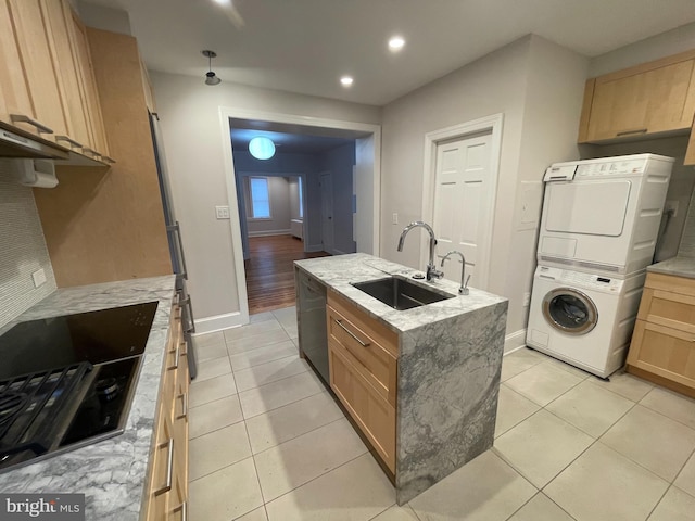 kitchen with light brown cabinets, a sink, cooktop, stacked washer and dryer, and stainless steel dishwasher