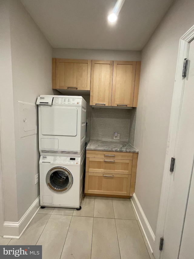 clothes washing area featuring light tile patterned floors, cabinet space, baseboards, and stacked washer and dryer