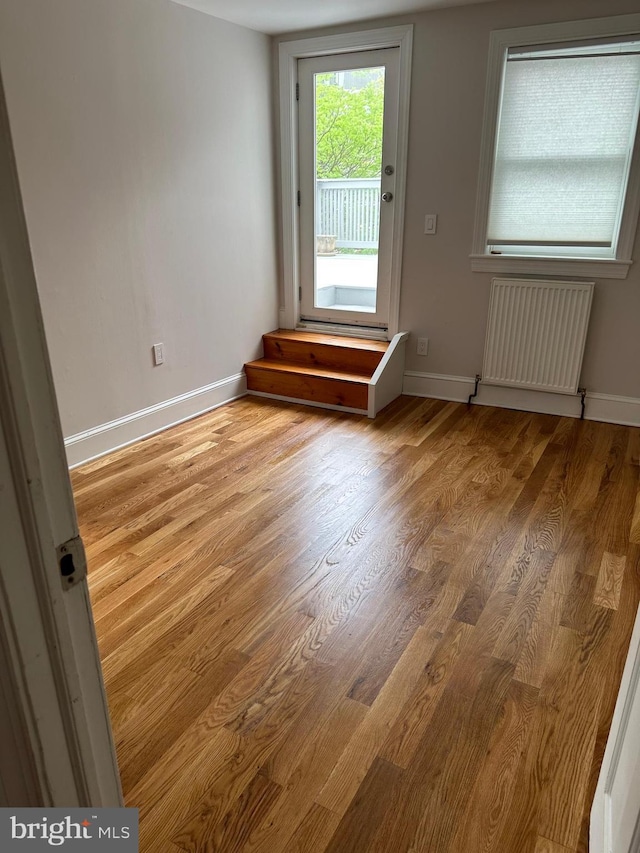 empty room with radiator heating unit, wood finished floors, and baseboards