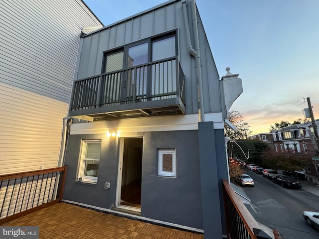 back of house at dusk featuring a balcony, board and batten siding, and stucco siding