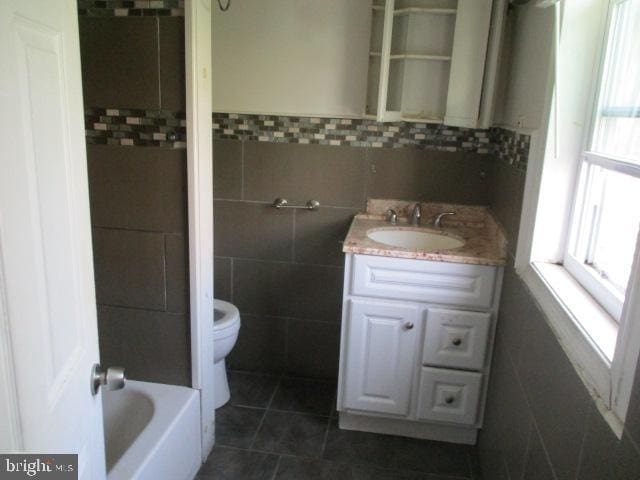 bathroom with toilet, tile walls, vanity, and a healthy amount of sunlight