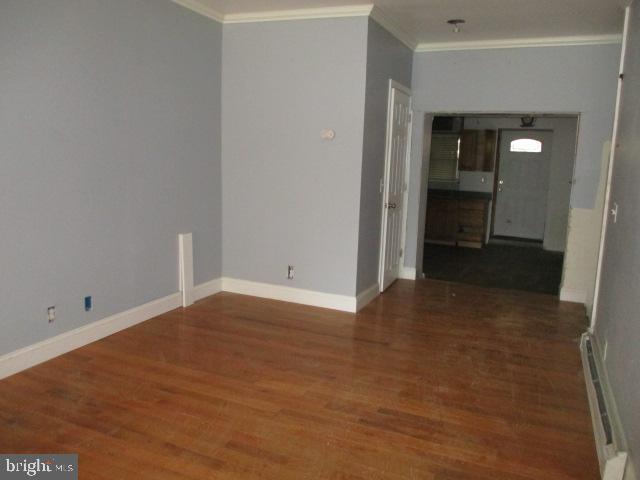 unfurnished room with crown molding, a baseboard heating unit, and dark hardwood / wood-style floors