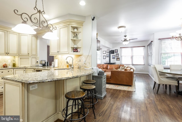 kitchen with hanging light fixtures, a peninsula, cream cabinetry, and a sink