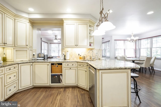 kitchen with a sink, a peninsula, cream cabinetry, and hanging light fixtures