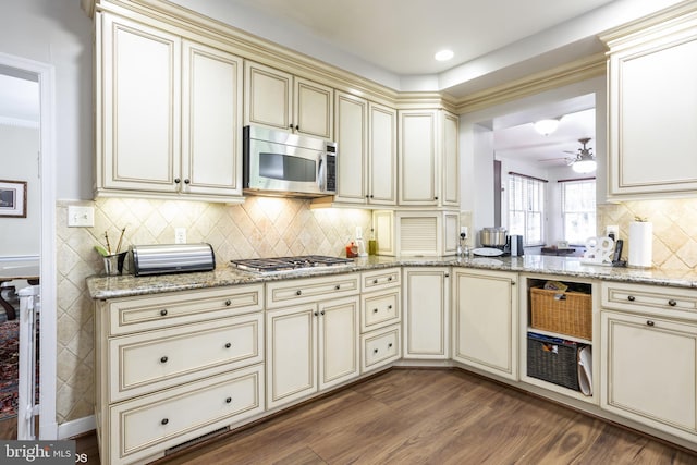 kitchen with appliances with stainless steel finishes, dark wood-type flooring, light stone counters, and cream cabinets