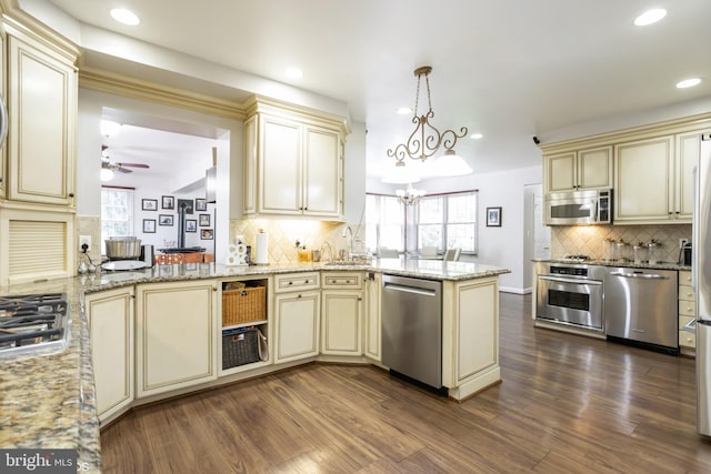 kitchen with tasteful backsplash, dark wood-type flooring, stainless steel appliances, kitchen peninsula, and cream cabinetry