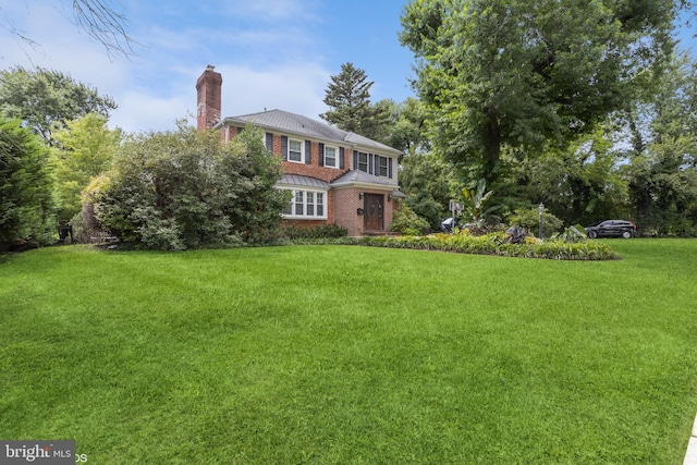 view of front of house featuring a front yard, brick siding, and a chimney