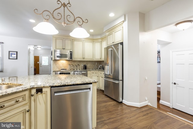 kitchen with hardwood / wood-style flooring, appliances with stainless steel finishes, light stone counters, cream cabinetry, and decorative backsplash