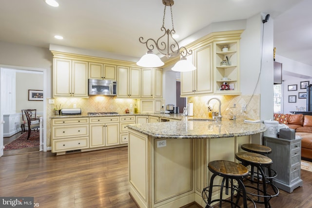 kitchen featuring hardwood / wood-style flooring, stainless steel appliances, kitchen peninsula, cream cabinetry, and tasteful backsplash