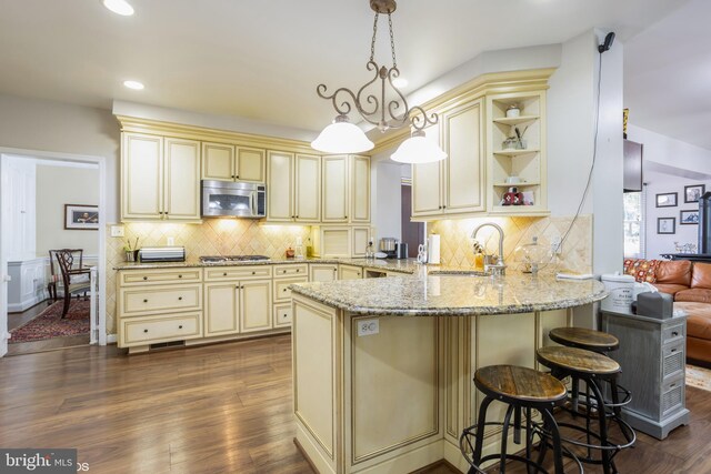 kitchen featuring appliances with stainless steel finishes, a breakfast bar, a peninsula, hanging light fixtures, and cream cabinets