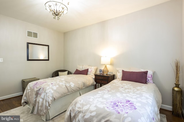 bedroom featuring an inviting chandelier, wood finished floors, visible vents, and baseboards