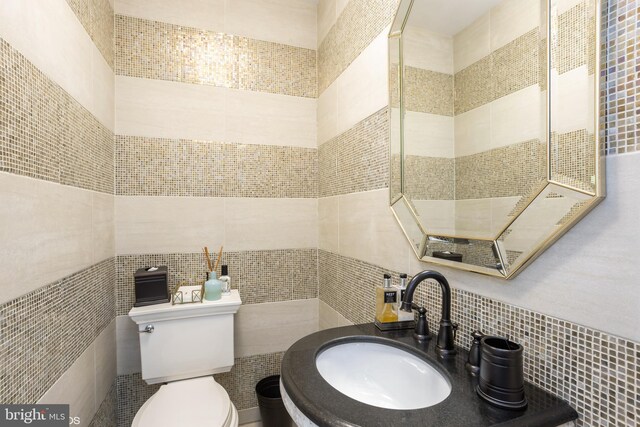 bathroom featuring tile walls, toilet, tasteful backsplash, and sink