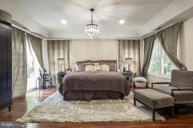 bedroom with a tray ceiling, a notable chandelier, and dark hardwood / wood-style flooring