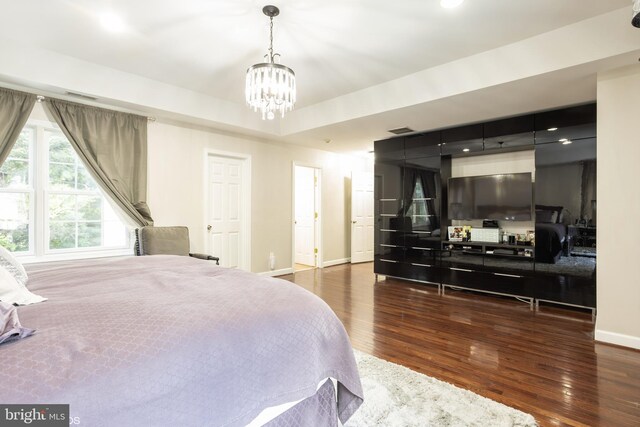 bedroom featuring dark wood-type flooring, a raised ceiling, and an inviting chandelier